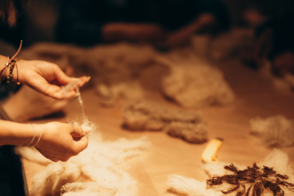 Hands drawing a thread of wool in a felting workshop